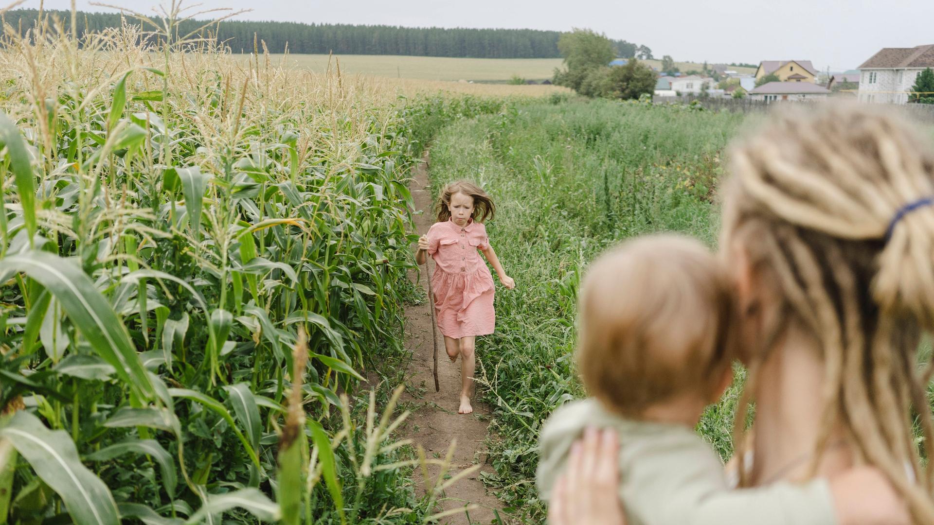 Ein Mädchen läuft auf einem Maisfeld seiner Mutter entgegen, im Hintergrund ist ein Dorf zu sehen. Ein Mädchen läuft auf einem Maisfeld seiner Mutter entgegen, im Hintergrund ist ein Dorf zu sehen.
