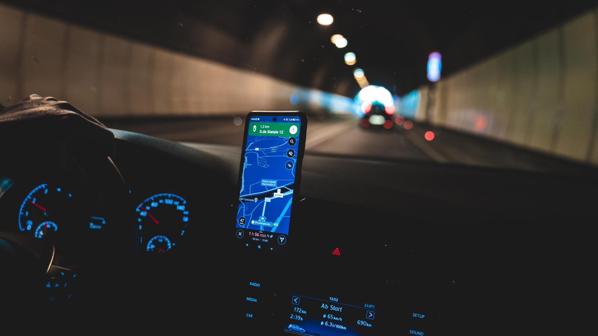 Ein Wagen fährt im Dunkeln durch einen Tunnel, im Cockpit des Fahrzeugs leuchten Navigation diverse Lichter sowie ein Smartphone mit der Google Maps App. Ein Wagen fährt im Dunkeln durch einen Tunnel, im Cockpit des Fahrzeugs leuchten Navigation diverse Lichter sowie ein Smartphone mit der Google Maps App.
