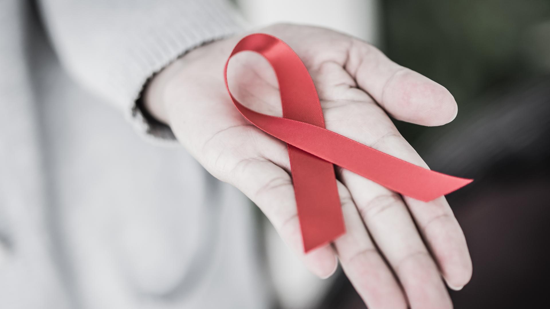 Eine Hand hält das rote AIDS Bändchen. Eine Hand hält das rote AIDS Bändchen.