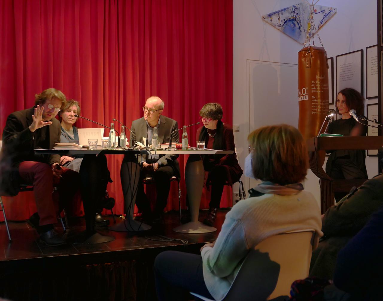 Auf einer Bühne sitzen Frieder von Ammon, Elke Schmitter, Jan Bürger und Barbara Wahlster gemeinsam am Tisch, rechts davon steht Birgitta Assheuer hinter einem Podium. Auf einer Bühne sitzen Frieder von Ammon, Elke Schmitter, Jan Bürger und Barbara Wahlster gemeinsam am Tisch, rechts davon steht Birgitta Assheuer hinter einem Podium.