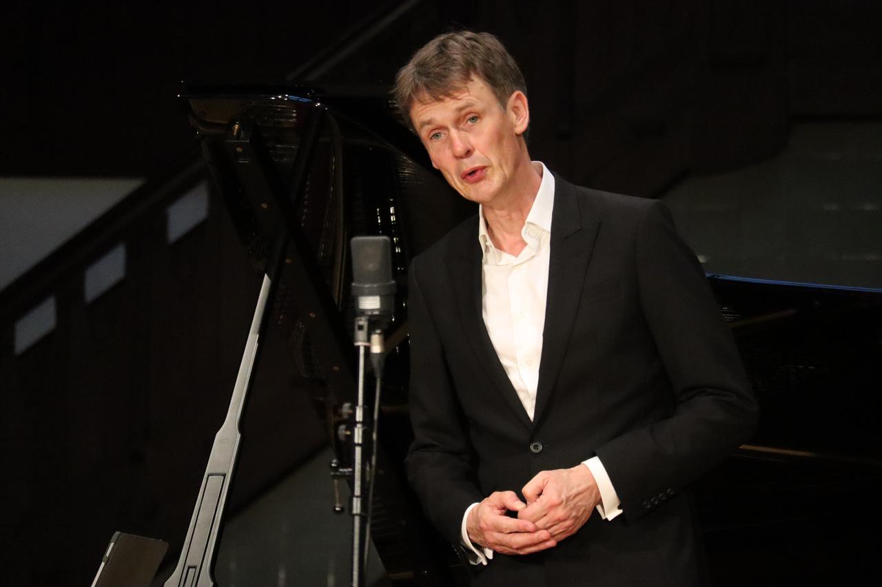 Ein Mann in weißem Hemd und schwarzem Jackett steht vor einem Mikrofon und singt konzentriert. Ein Mann in weißem Hemd und schwarzem Jackett steht vor einem Mikrofon und singt konzentriert.