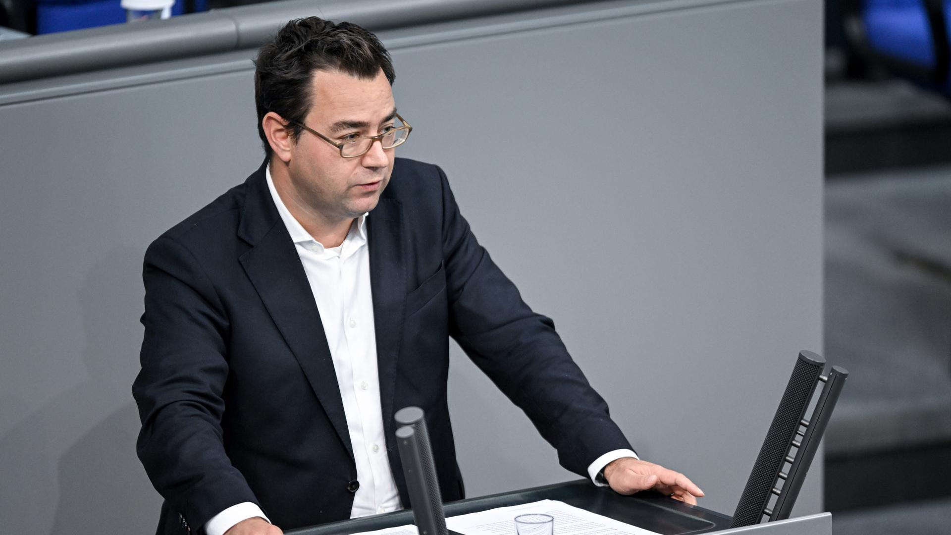 Sebastian Schäfer steht am Rednerpult im Bundestag. Er trägt ein weißes Hemd ohne Krawatte und ein schwarzes Sakko.