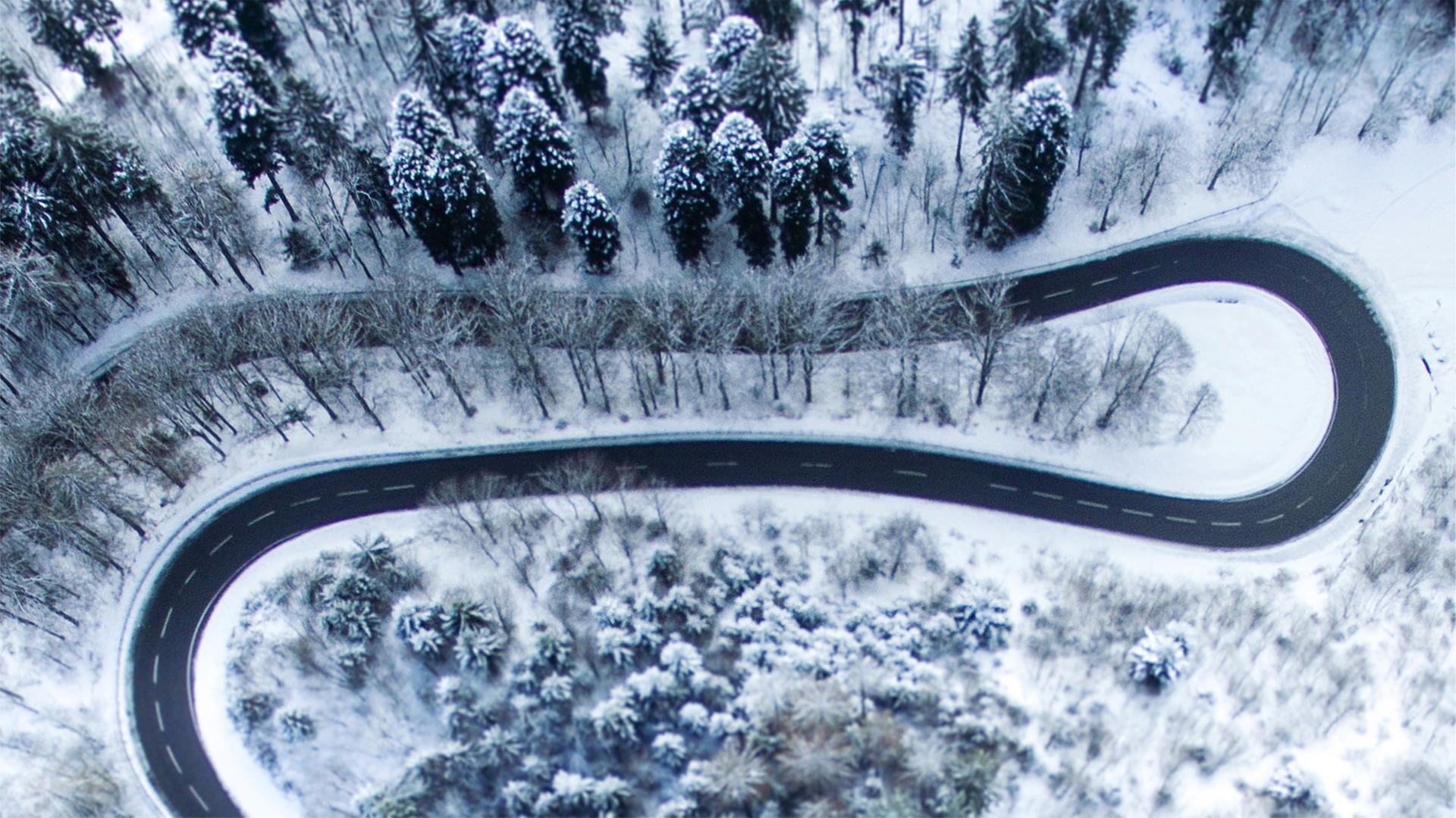 Eine sich schlängelnde Straße in verschneiter Waldlandschaft aus der Vogelperspektive. Eine sich schlängelnde Straße in verschneiter Waldlandschaft aus der Vogelperspektive.