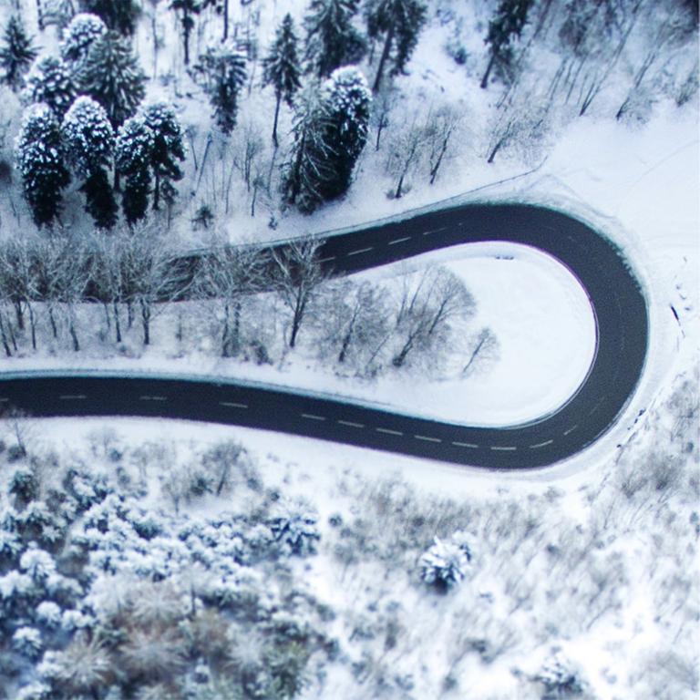 Eine sich schlängelnde Straße in verschneiter Waldlandschaft aus der Vogelperspektive. Eine sich schlängelnde Straße in verschneiter Waldlandschaft aus der Vogelperspektive.