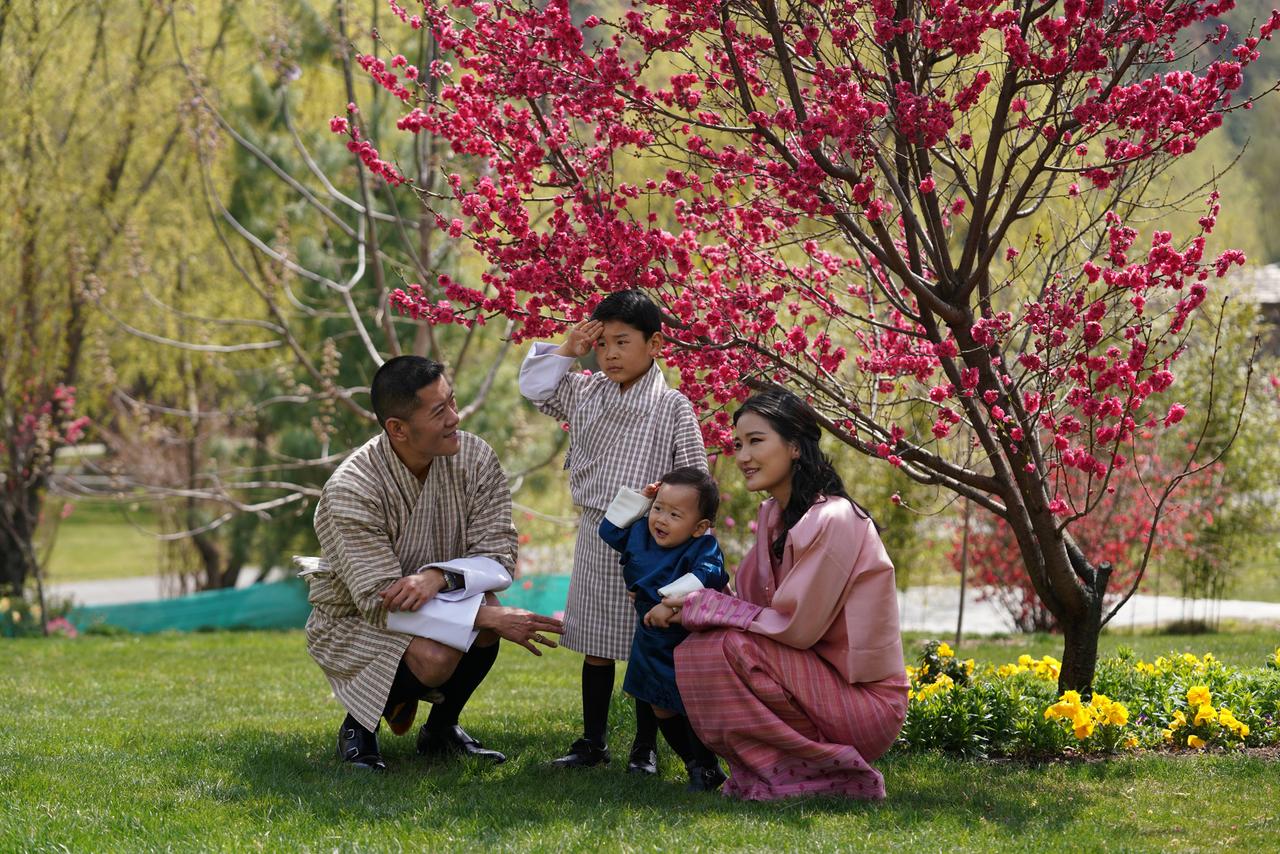 Ein Paar und seine beiden kleinen Kinder hocken unter blühenden Bäumen in einem grünen Park.