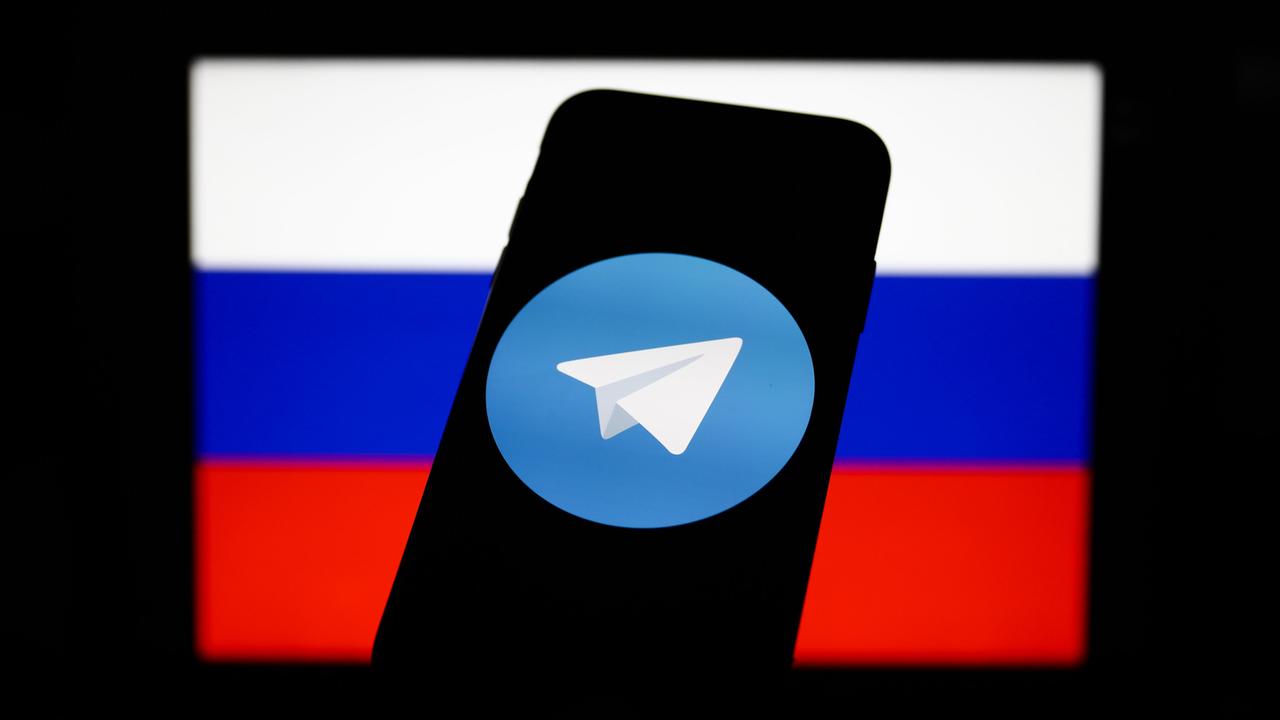 Das Logo des Messengerdienstes Telegram auf dem Bildschirm eines Mobiltelefons, eingebettet in die russische Fahne. 
