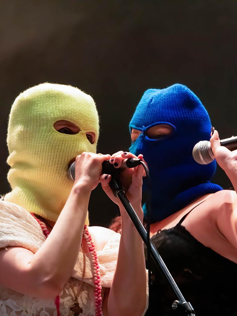 Zwei Frauen stehen auf einer Bühnen und halten ein Mikro in der Hand. Ihre Gesichter kann man nicht erkennen, da sie eine gelbe beziehungsweise blaue Sturmhaube über den Kopf gezogen haben.