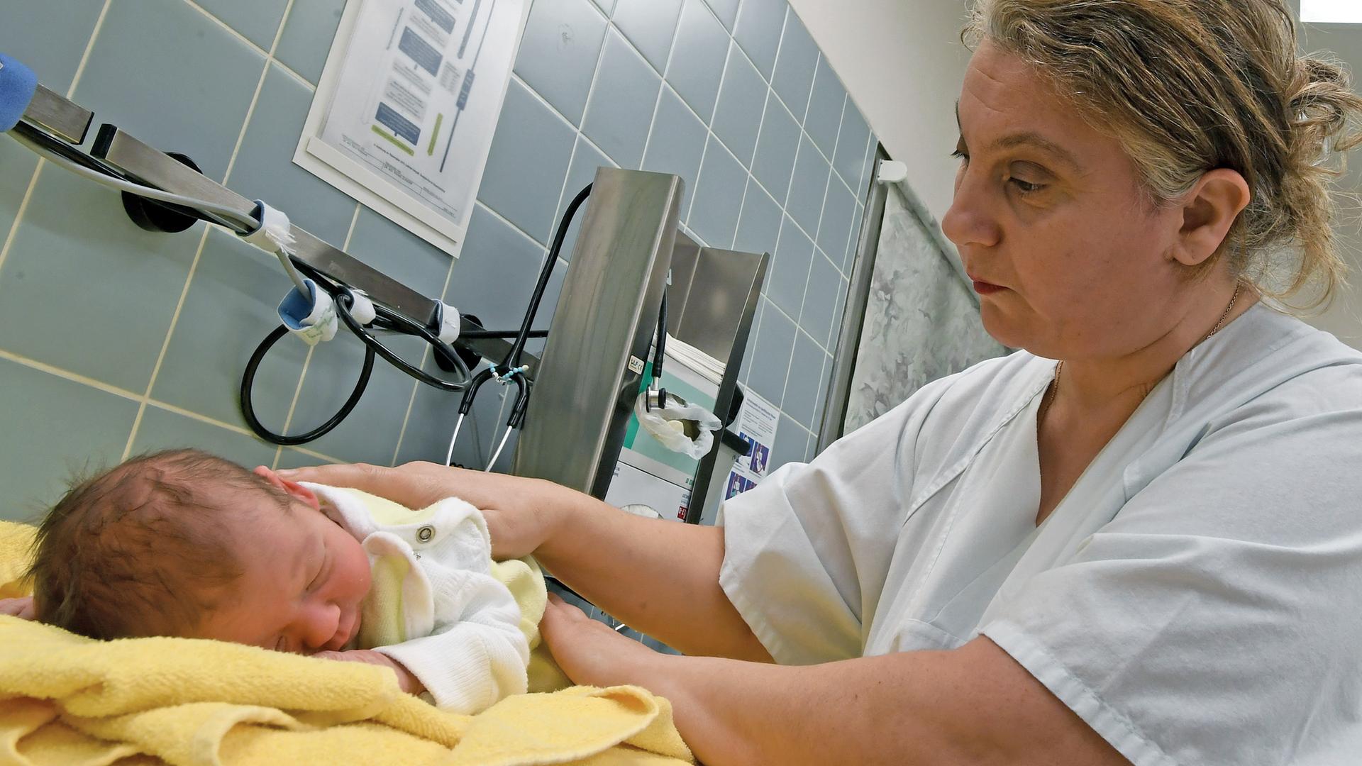 Eine Hebamme versorgt ein wenige Tage altes Neugeborenes in einer Klinik für Geburtshilfe in Niedersachsen