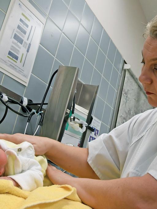 Eine Hebamme versorgt ein wenige Tage altes Neugeborenes in einer Klinik für Geburtshilfe in Niedersachsen