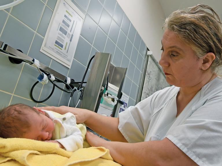 Eine Hebamme versorgt ein wenige Tage altes Neugeborenes in einer Klinik für Geburtshilfe in Niedersachsen