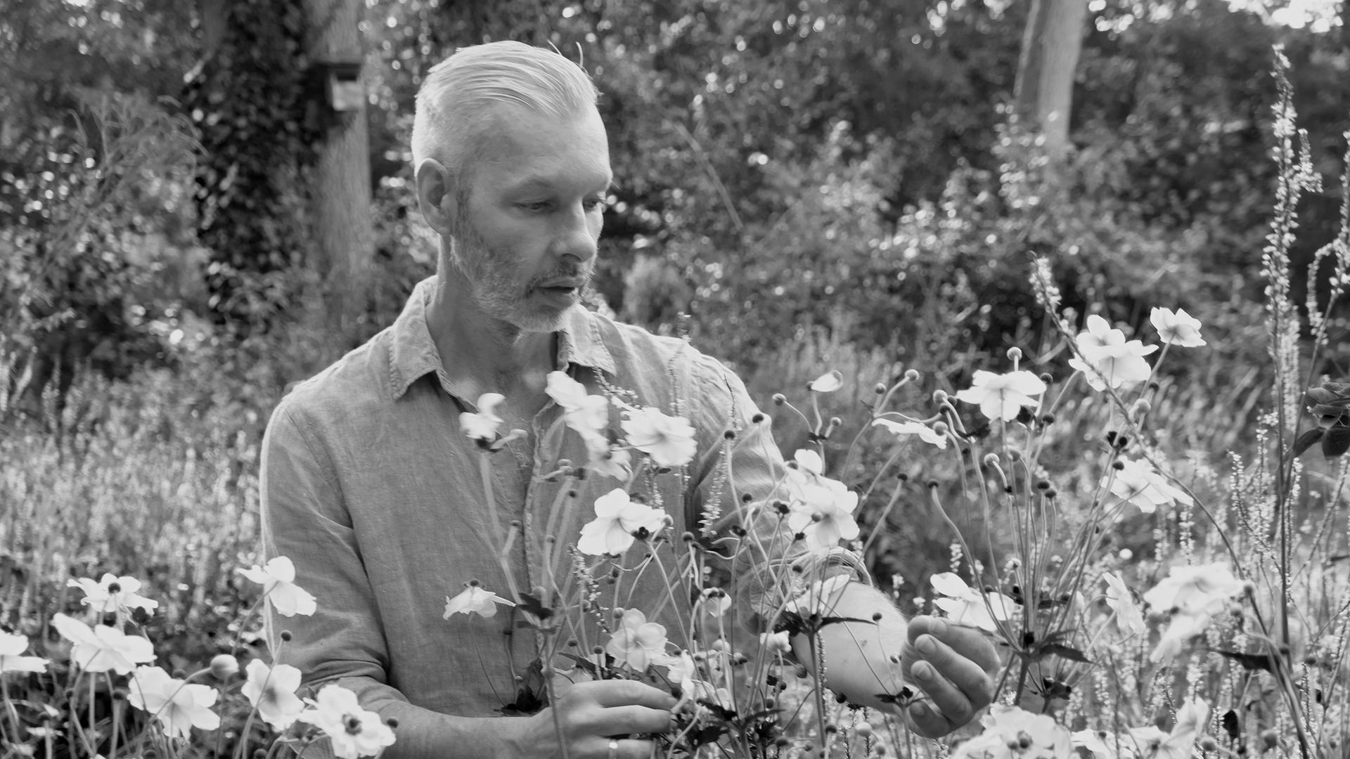 Schwarzweißfoto von Rainer Elstermann, der Wildblumen im Garten betrachtet.