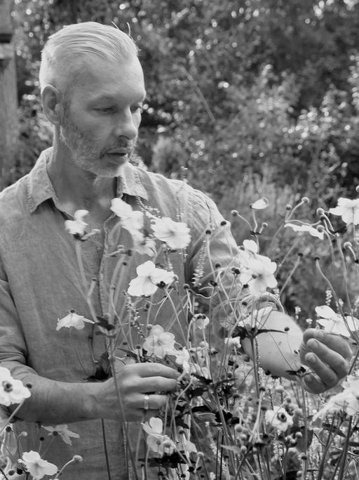 Schwarzweißfoto von Rainer Elstermann, der Wildblumen im Garten betrachtet.