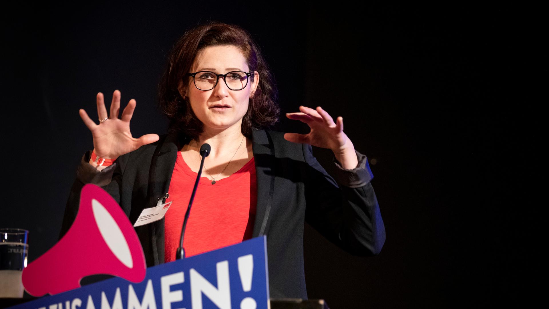 Eine Frau steht an einem Mikrofon und hebt die Hände. Es ist die Publizistin Ferda Ataman. Eine Frau steht an einem Mikrofon und hebt die Hände. Es ist die Publizistin Ferda Ataman.