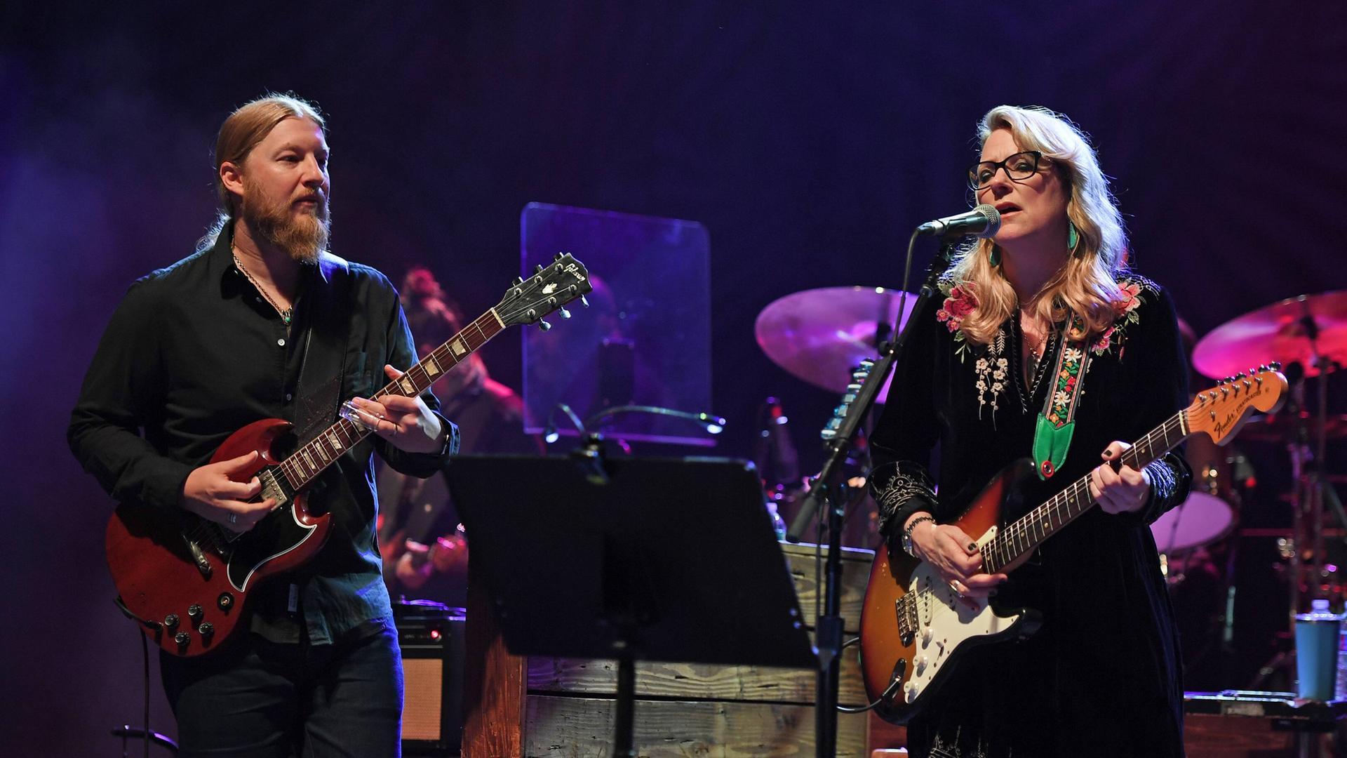 Derek Trucks and Susan Tedeschi stehen performend auf einer Bühne, während beide Gitarre spielen und sie zusätzlich singt. Derek Trucks and Susan Tedeschi stehen performend auf einer Bühne, während beide Gitarre spielen und sie zusätzlich singt.