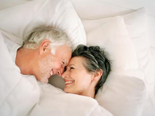 Ein älteres Paar lacht einander im Bett an.