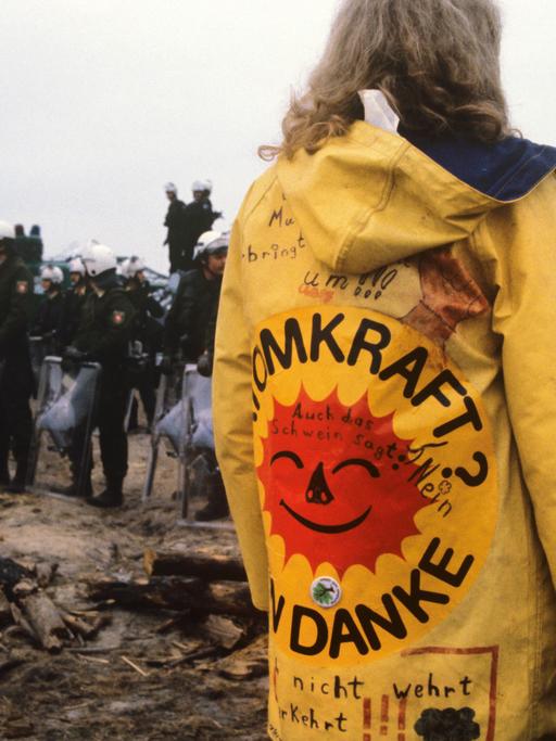 Eine Frau mit einem gelben Regenmantel und der Aufschrift "Atomkraft, nein danke!" ist zu sehen im Hüttendorf in Gorleben, 1980.