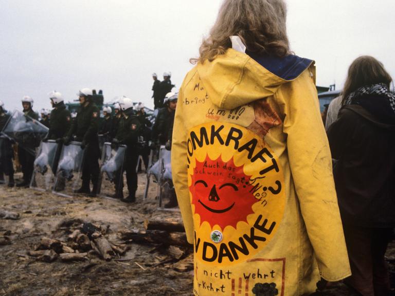 Eine Frau mit einem gelben Regenmantel und der Aufschrift "Atomkraft, nein danke!" ist zu sehen im Hüttendorf in Gorleben, 1980.