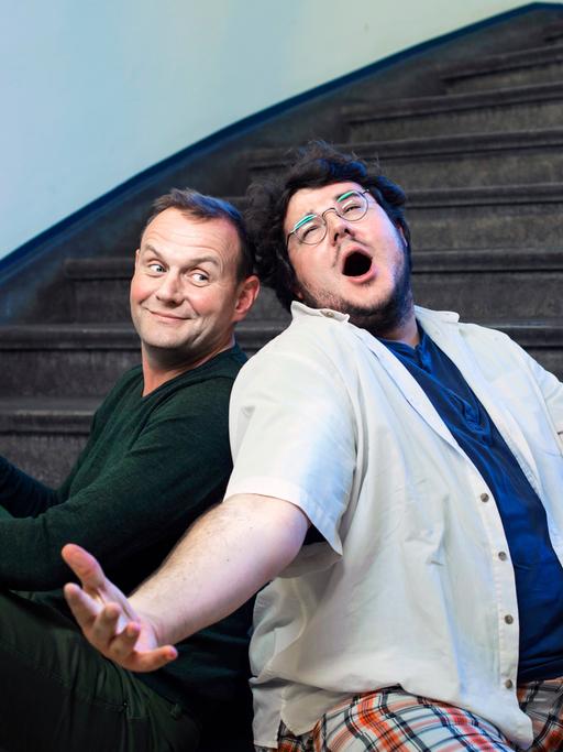 Devid Striesow und Axel Rahnisch sitzen auf einer Treppe, Rahnisch singt.