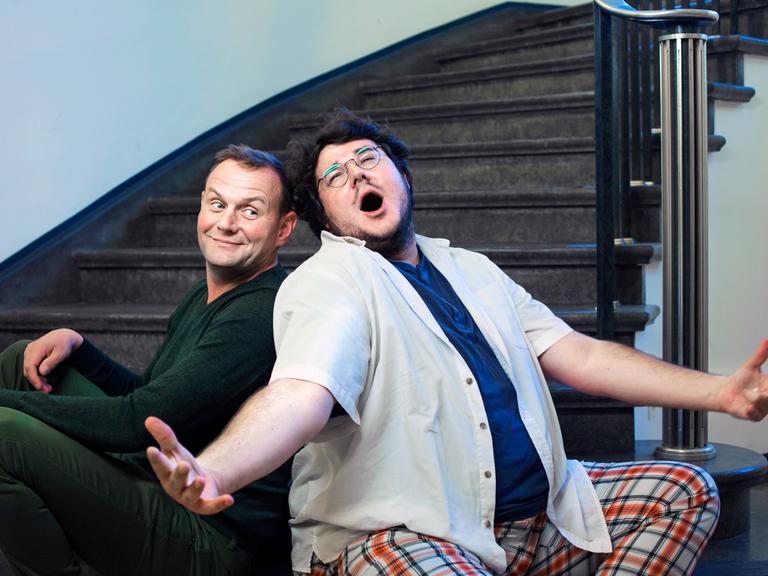 Devid Striesow und Axel Rahnisch sitzen auf einer Treppe, Rahnisch singt.