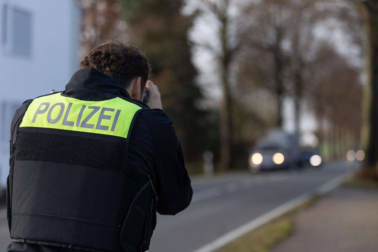  Ein Beamter der Polizei steht mit einem Laser für die Geschwindigkeitsmessung von Fahrzeugen an einer Straße.