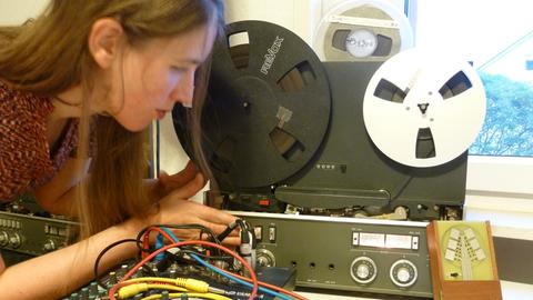 Eine junge Frau hantiert an Steckfeldern vor Tonbandmaschinen
