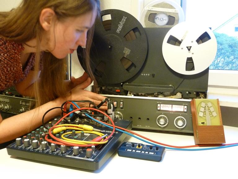 Eine junge Frau hantiert an Steckfeldern vor Tonbandmaschinen