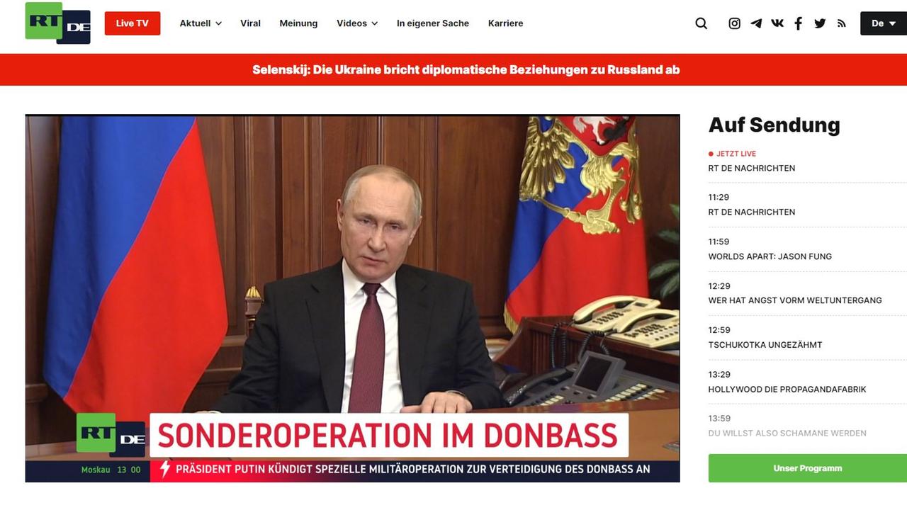 Russlands Präsident Wladimir Putin an einem Schreibtisch, im Hintergrund zwei russische Flaggen 
