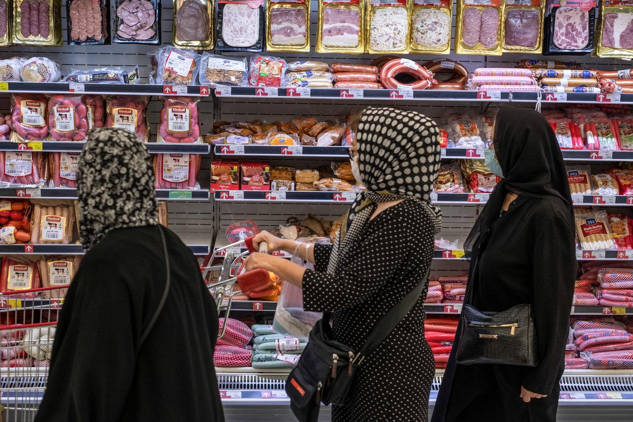 Frauen stehen vor einem mit Wurstwaren gefüllten Kühlregal in einem Supermarkt. Frauen stehen vor einem mit Wurstwaren gefüllten Kühlregal in einem Supermarkt.