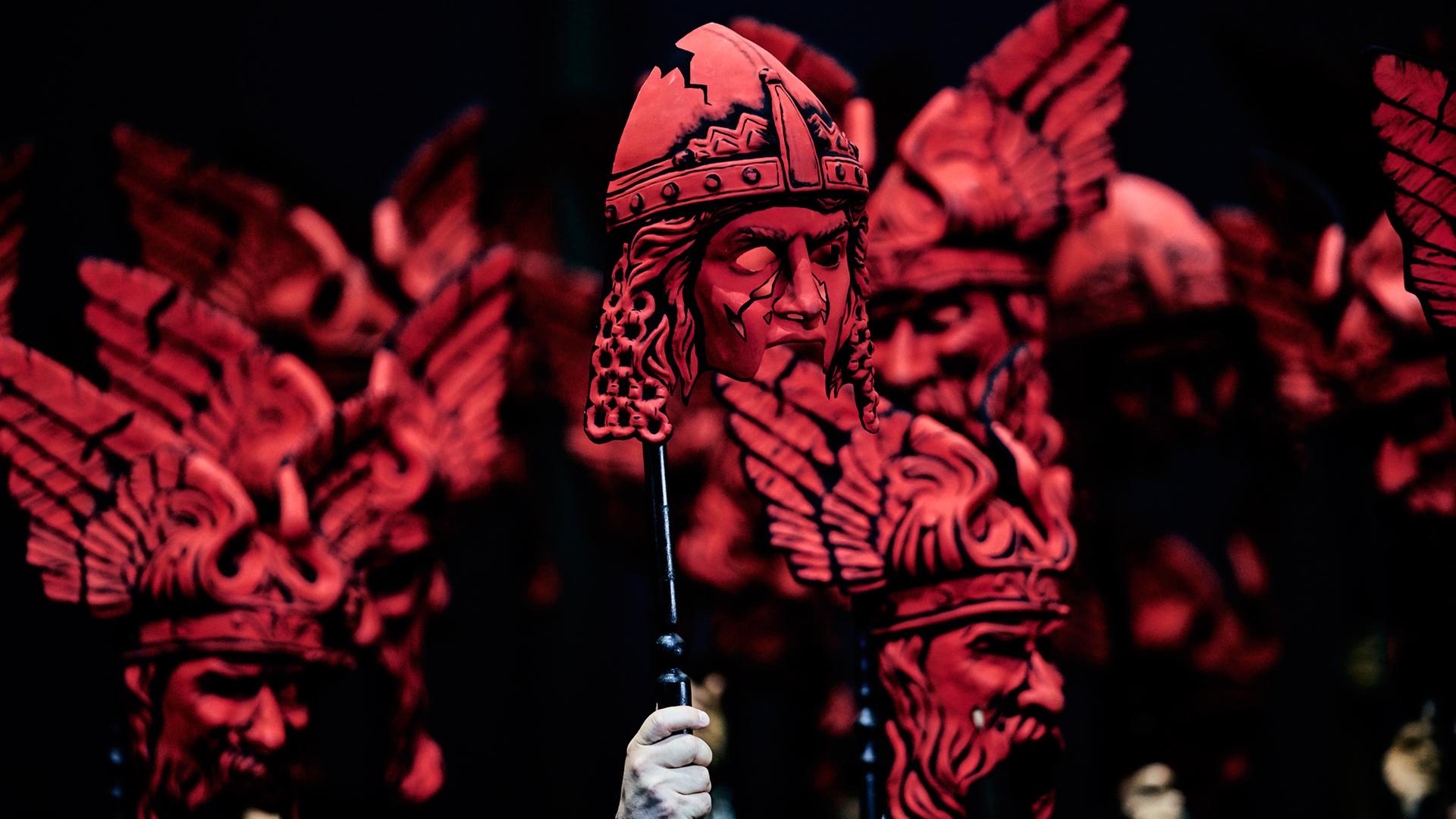 Auf der Bühne halten Darsteller bei der "Götterdämmerung" rote Masken in die Höhe. Auf der Bühne halten Darsteller bei der "Götterdämmerung" rote Masken in die Höhe.
