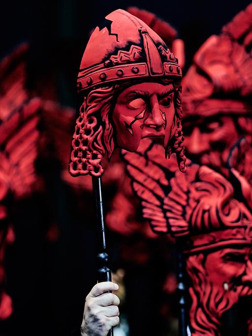 Auf der Bühne halten Darsteller bei der "Götterdämmerung" rote Masken in die Höhe.