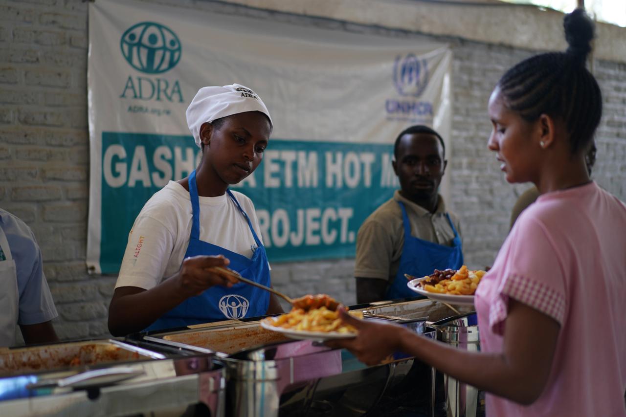 Eine Küchenhilfe tut an einem Tresen anstehenden Menschen Essen auf: im Flüchtlingscamp Gashora in Ruanda.