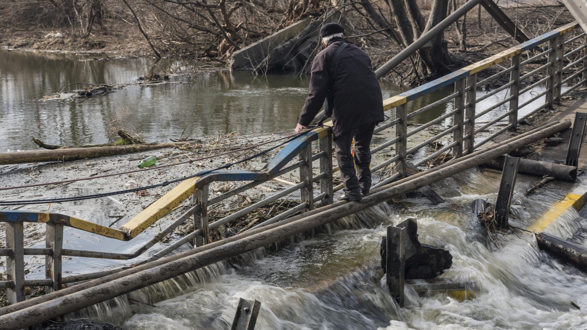 Ein älterer Mann steht auf einer beschädigten Brücke über einem Fluss. Ein älterer Mann steht auf einer beschädigten Brücke über einem Fluss.