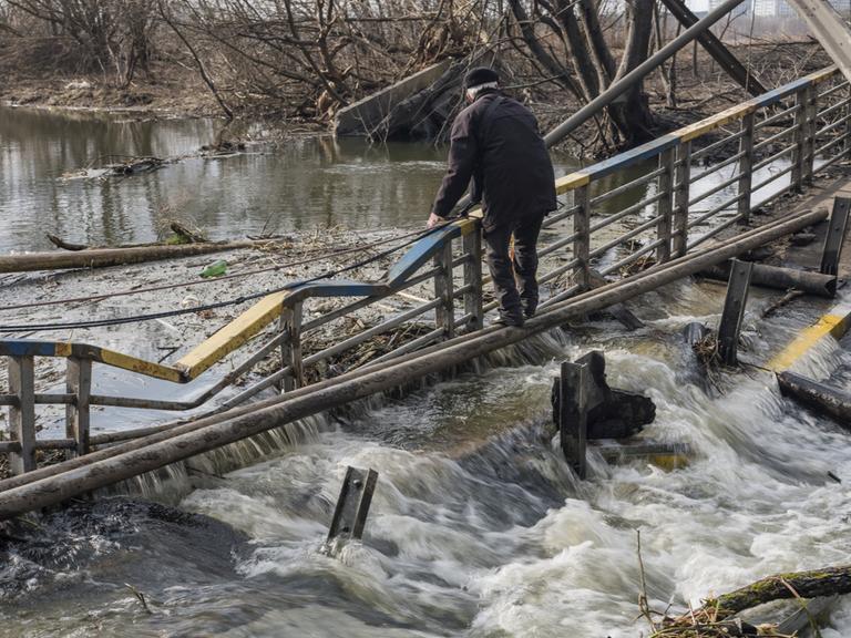 Ein älterer Mann steht auf einer beschädigten Brücke über einem Fluss.