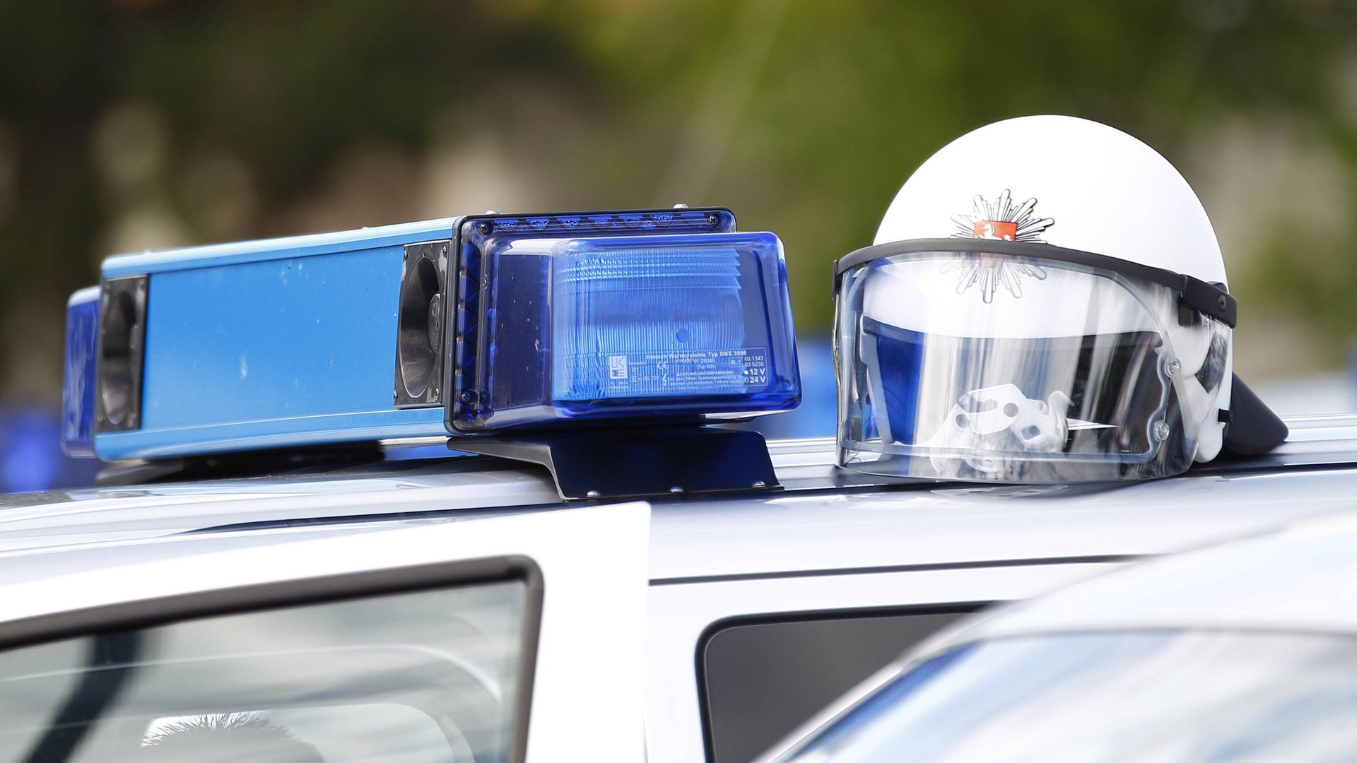 Auf dem Dach eines Polizeiautos mit Blaulichtanlage liegt ein Schutzhelm. Auf dem Dach eines Polizeiautos mit Blaulichtanlage liegt ein Schutzhelm.