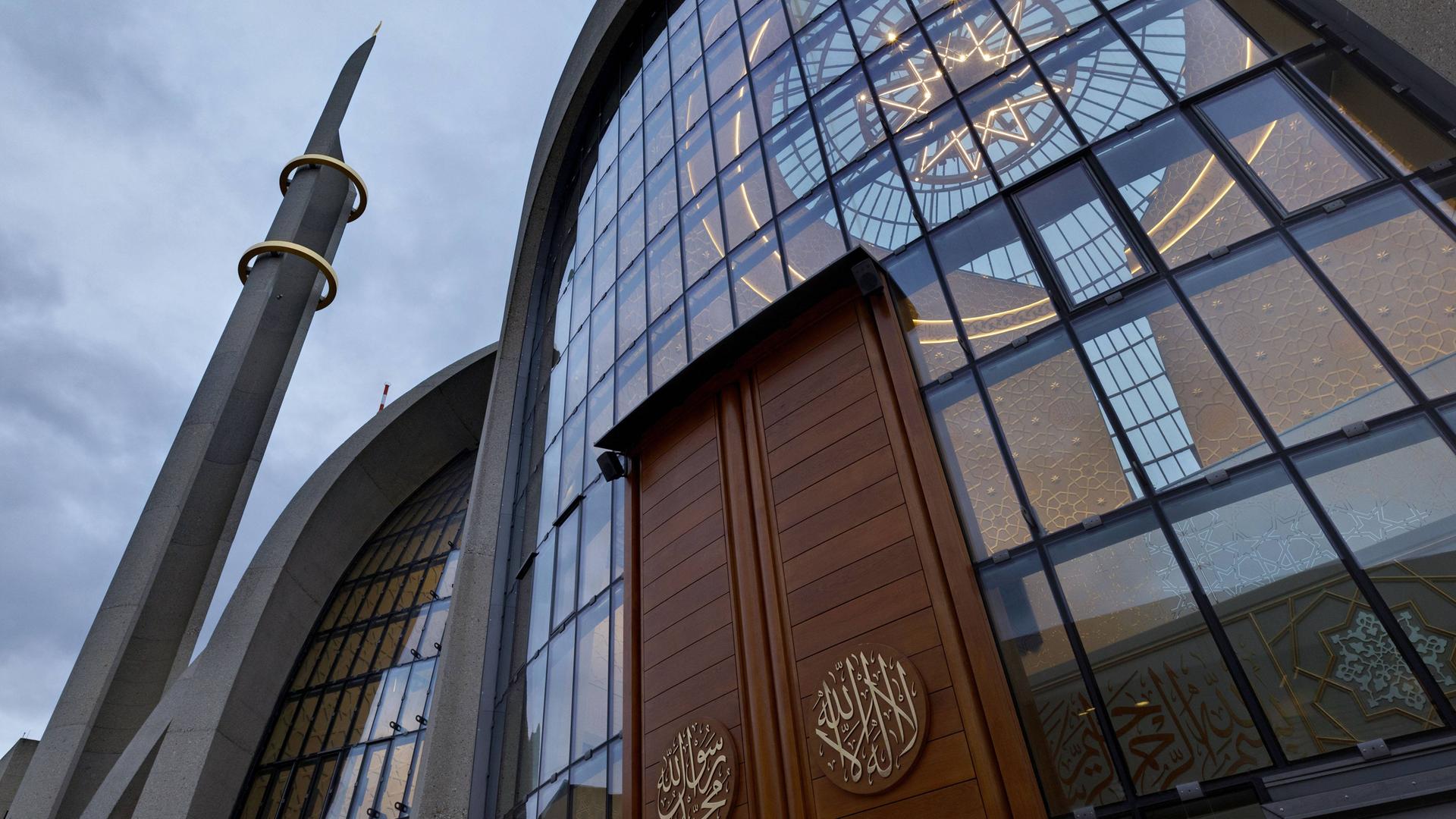 Blick auf die Zentralmoschee in Köln. In der Mitte des Bildes ist die Eingangstür zu sehen, rechts danebem blickt die Kamera in das Innere der Zentralmoschee in Köln-Ehrenfeld. Die oben gläserne Kuppel ist zu sehen. Blick auf die Zentralmoschee in Köln. In der Mitte des Bildes ist die Eingangstür zu sehen, rechts danebem blickt die Kamera in das Innere der Zentralmoschee in Köln-Ehrenfeld. Die oben gläserne Kuppel ist zu sehen.