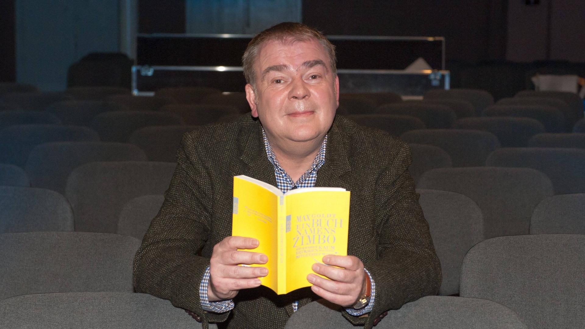 Max Goldt sitzt mit einem gelben Buch in der Hand Max Goldt sitzt mit einem gelben Buch in der Hand