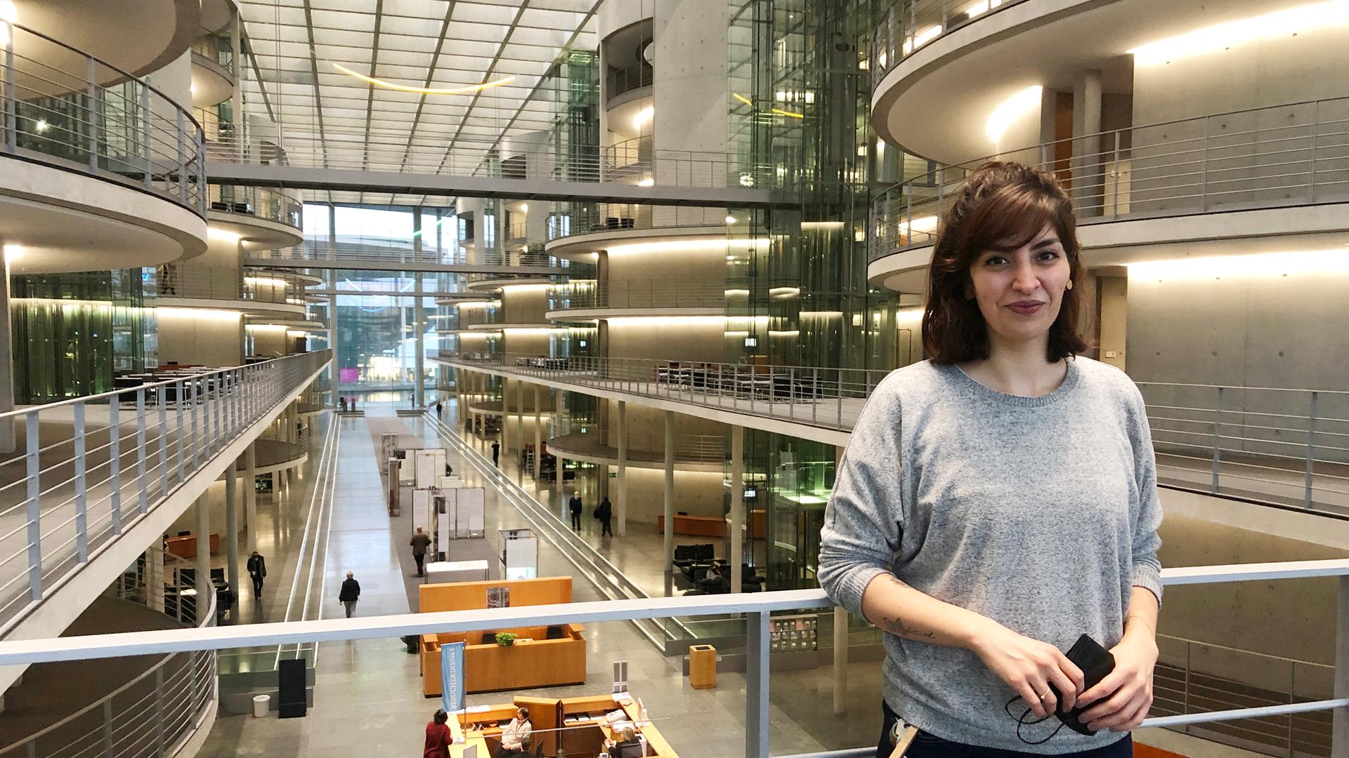 Ein junge Frau mit halblangen dunklen Haaren, in Jeans und grauem Pullover, steht in der Halle des Deutschen Bundestages. Ein junge Frau mit halblangen dunklen Haaren, in Jeans und grauem Pullover, steht in der Halle des Deutschen Bundestages.