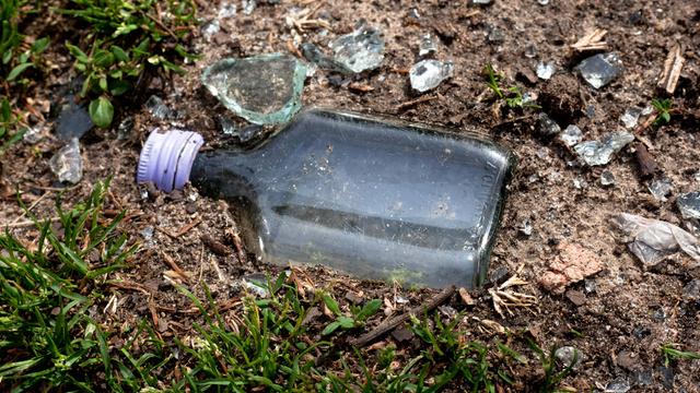 Eine leere kleine Schnapsflasche liegt ohne Etikett, plattgetreten, in der Erde.