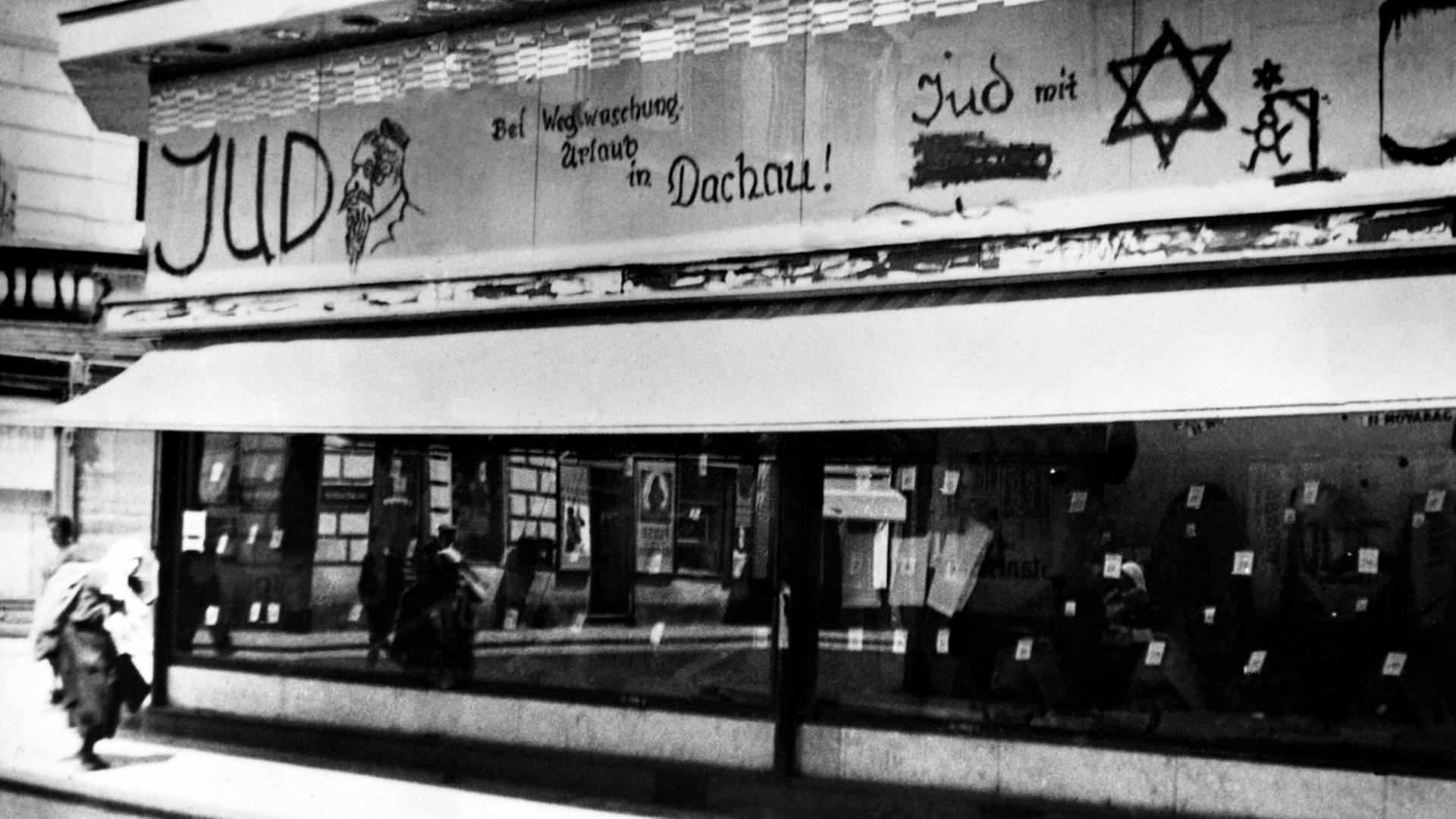 Im jüdischen Viertel in Wien, 1938. Beleidigungen und Drohungen stehen mit schwarzer Schrift über dem Schaufenster eines Geschäftes: "Bei Wegwaschung Urlaub in Dachau" und ein Männchen hängt an einem Galgen.