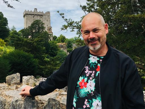 Alfons Mühlenbrock steht mit dem Arm an eine Mauer gestützt. Im Hintergrund ist der Turm einer Burg erkennbar. Alfons Mühlenbrock steht mit dem Arm an eine Mauer gestützt. Im Hintergrund ist der Turm einer Burg erkennbar.