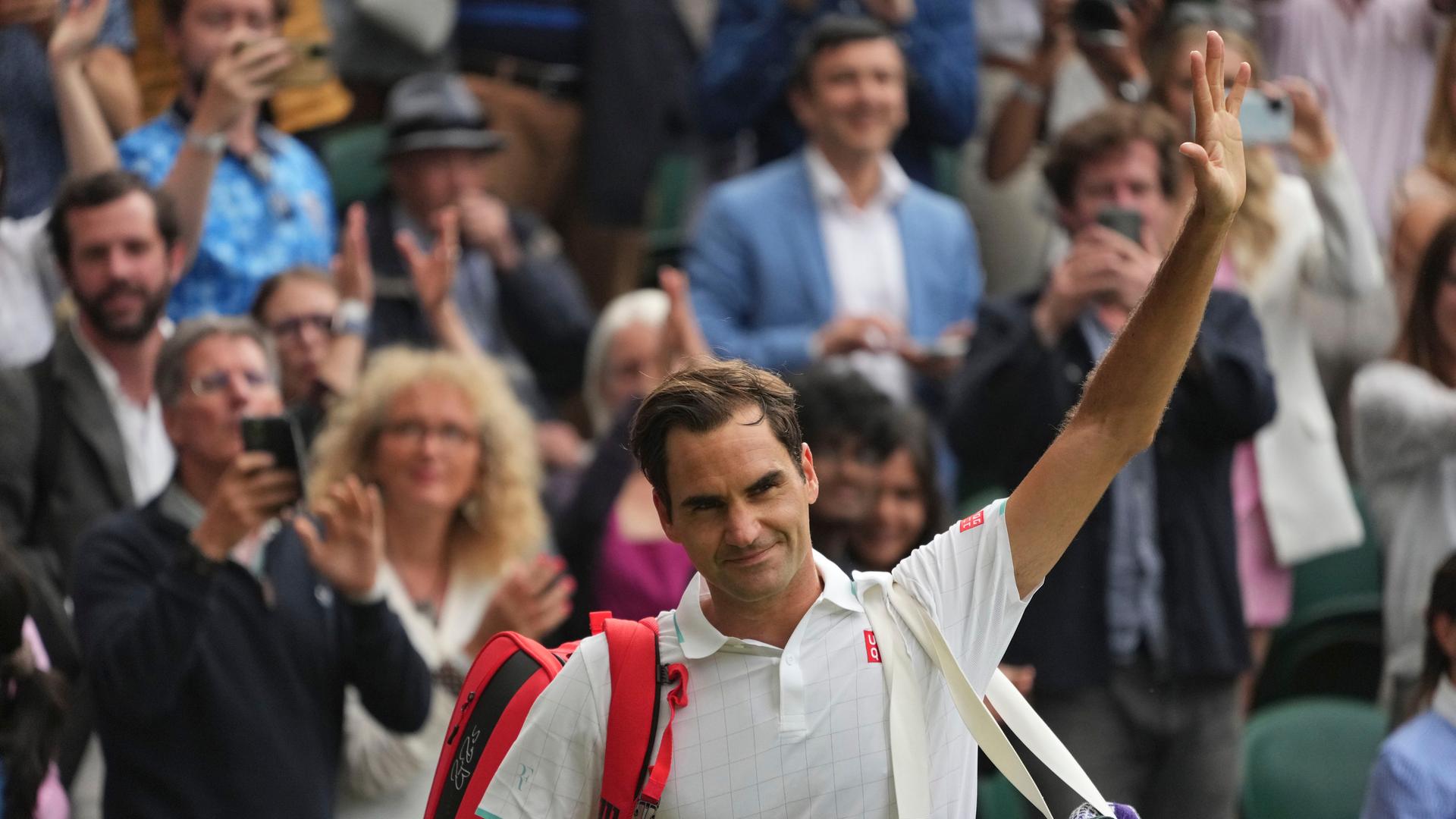 Ein Tennis-Spieler trägt zwei Taschen. Er winkt. Ein Tennis-Spieler trägt zwei Taschen. Er winkt.