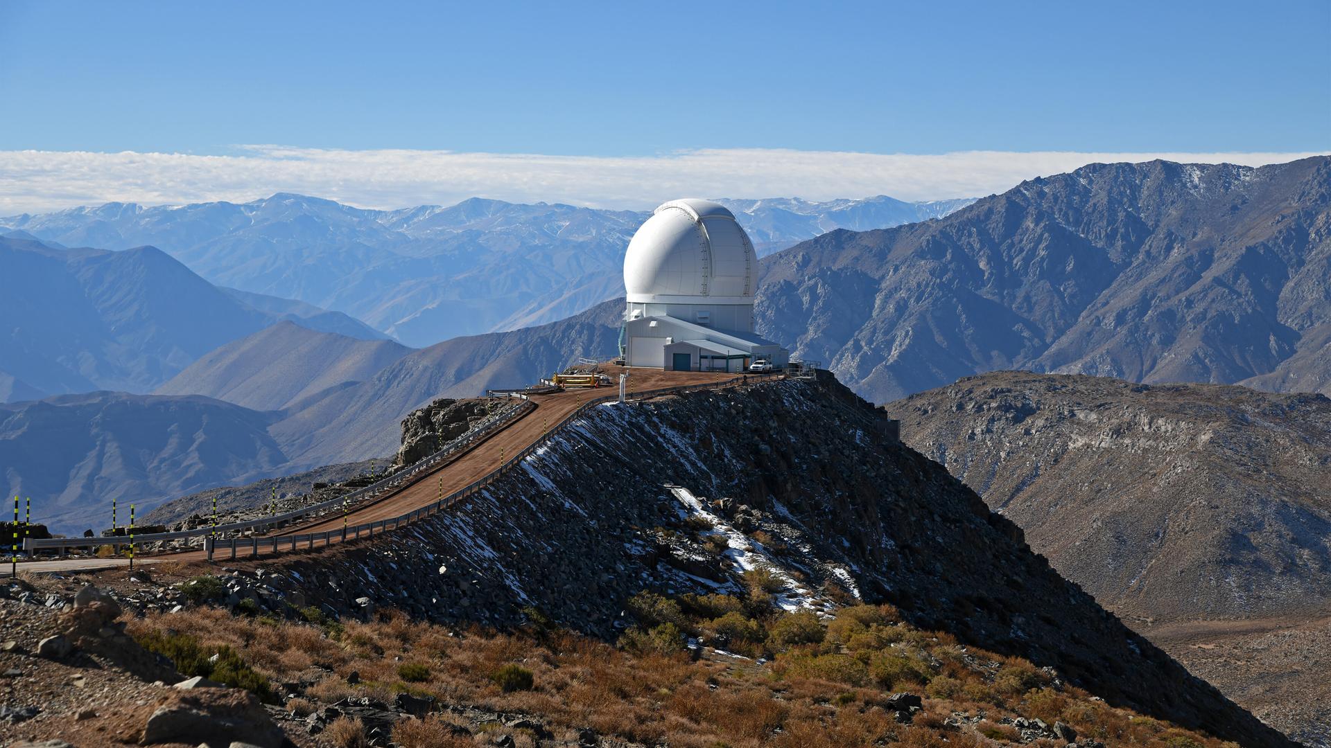 Observatorium in Chile auf dem Berg Cerro Pachon mit einer Berglandschaft und blauem Himmel im Hintergrund. 