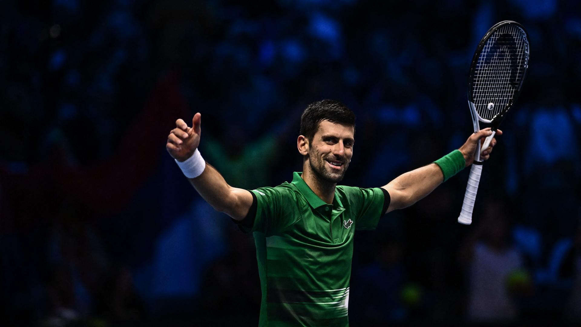 Der Tennis-Spieler Novak Djokovic hebt beide Arme in die Höhe. Er hält seinen Tennis-Schläger in der Hand. Der Tennis-Spieler Novak Djokovic hebt beide Arme in die Höhe. Er hält seinen Tennis-Schläger in der Hand.