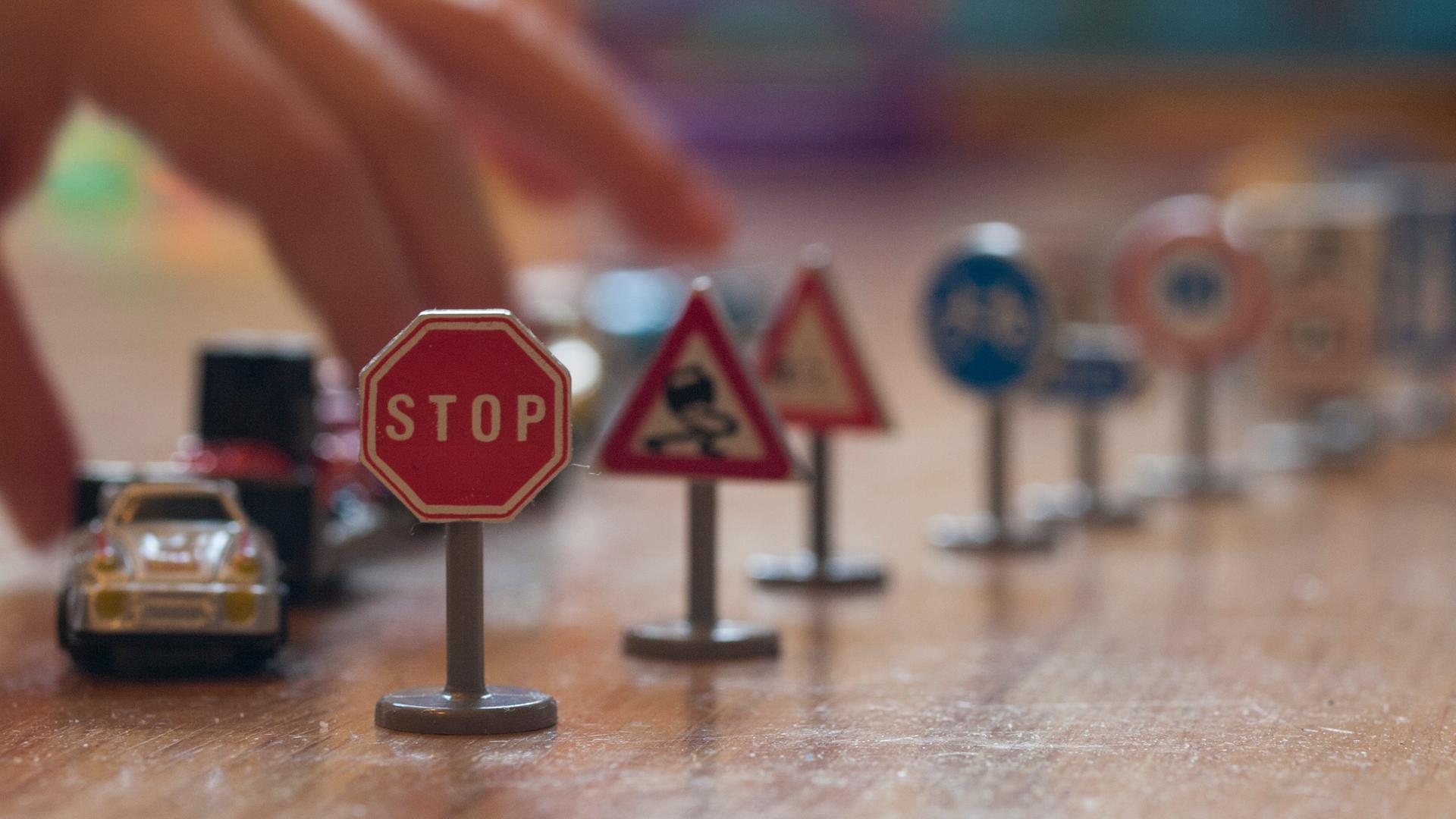 Eine Hand und ein Spielzeugauto sowie diverse Verkehrsschilder im Mini-Format. Eine Hand und ein Spielzeugauto sowie diverse Verkehrsschilder im Mini-Format.