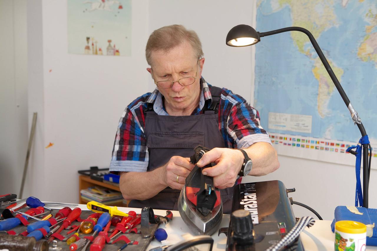 Ein Mann arbeitet in einem Reparaturcafé an einem Bügeleisen. Ein Mann arbeitet in einem Reparaturcafé an einem Bügeleisen.
