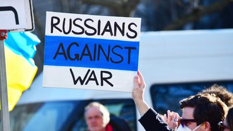 Ein offensichtlich russischer Teilnehmer hält auf einer Demo ein Plakat mit der Aufschrift "Russen gegen Krieg" in Händen