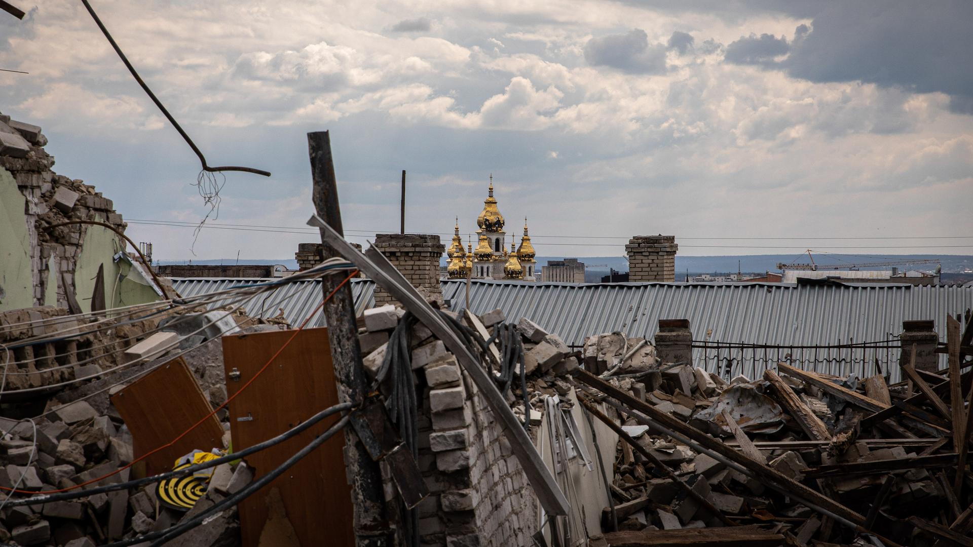 Die goldenen Türme eines orthodoxen Klosters sind im Hintergrund einer zerbombten Stadt zu sehen