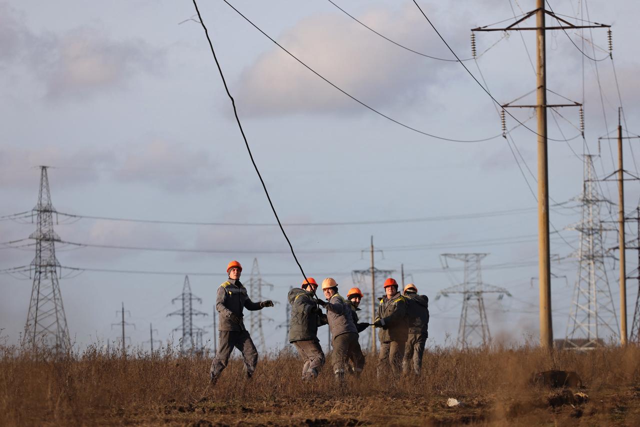 Arbeiter mit Helmen ziehen gemeinsam an einem kaputten Stromkabel, das von einem Strommast herunterhängt.