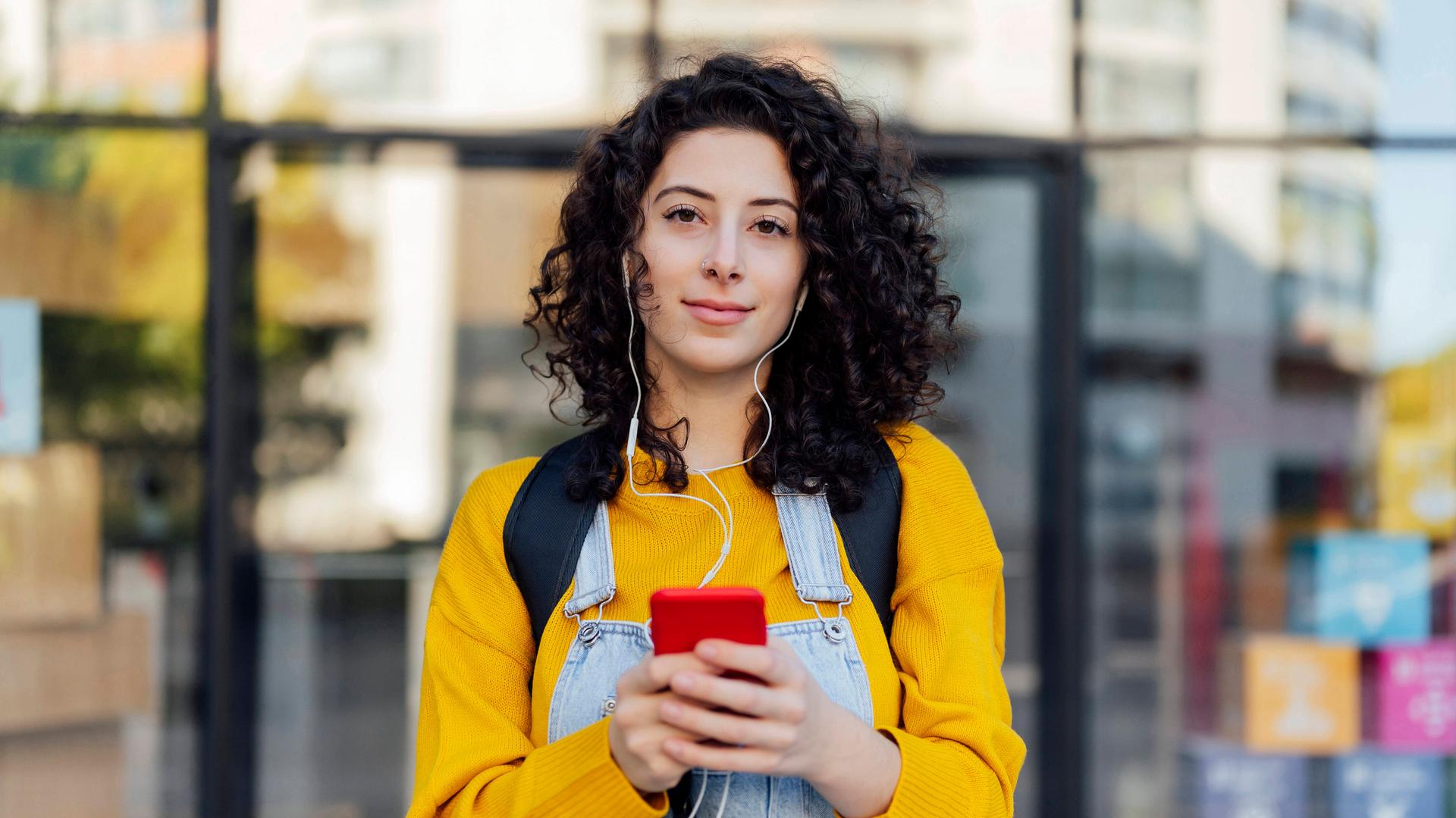 Eine junge Frau hat Kopfhörer auf, die mit ihrem Smartphone verbunden sind, das sie in der Hand hält
