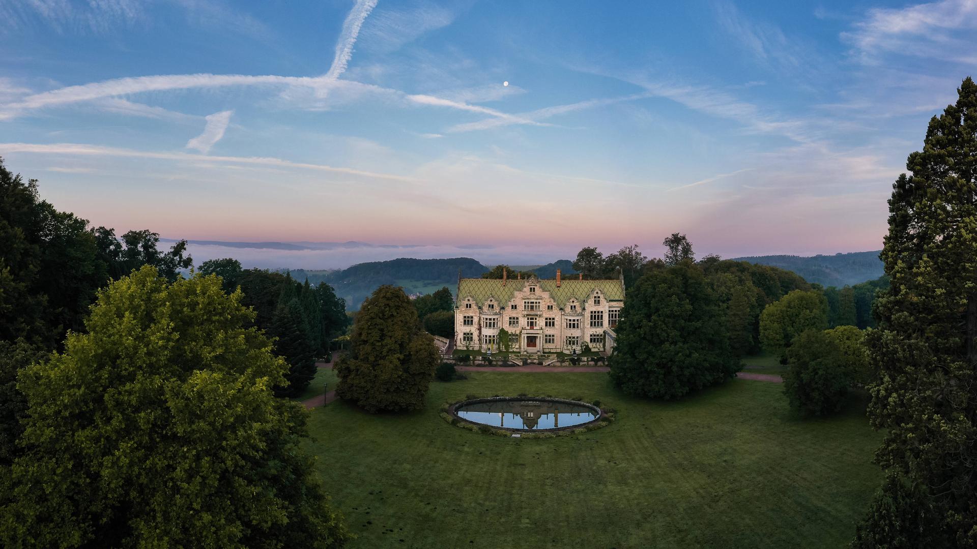 Drohnenblick über das Schloss  und den Landschaftspark Altenstein mit gefärbtem Abendhimmel.